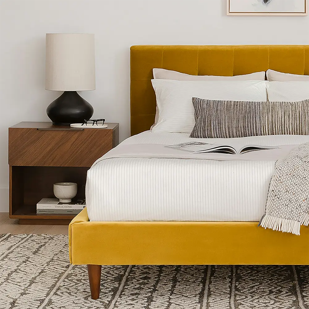 Yellow bed with white bedding and a wooden nightstand in a bedroom setting.