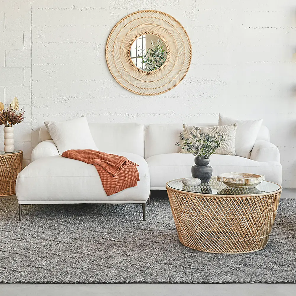 Modern living room with white sofa, wicker coffee table, and decorative mirror.