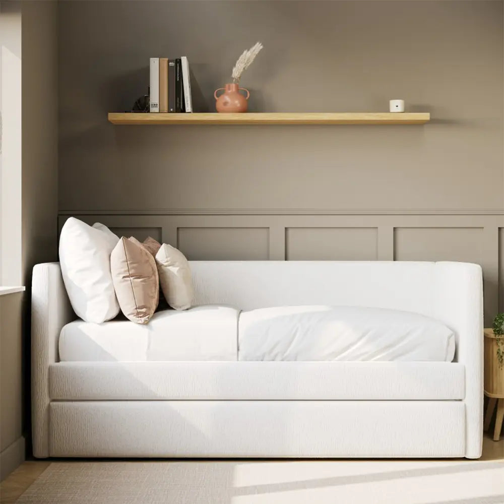 White sofa bed with pillows in a room with a shelf and neutral walls
