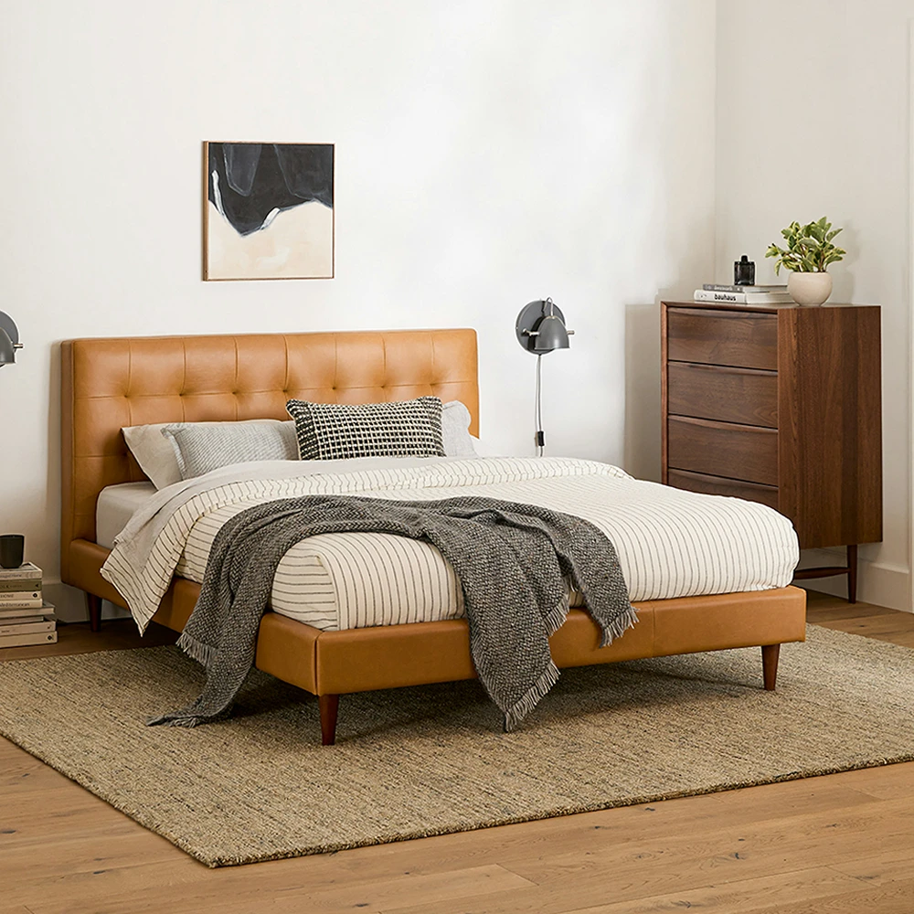 Modern bedroom with a brown leather bed, wooden dresser, and abstract art on the wall.