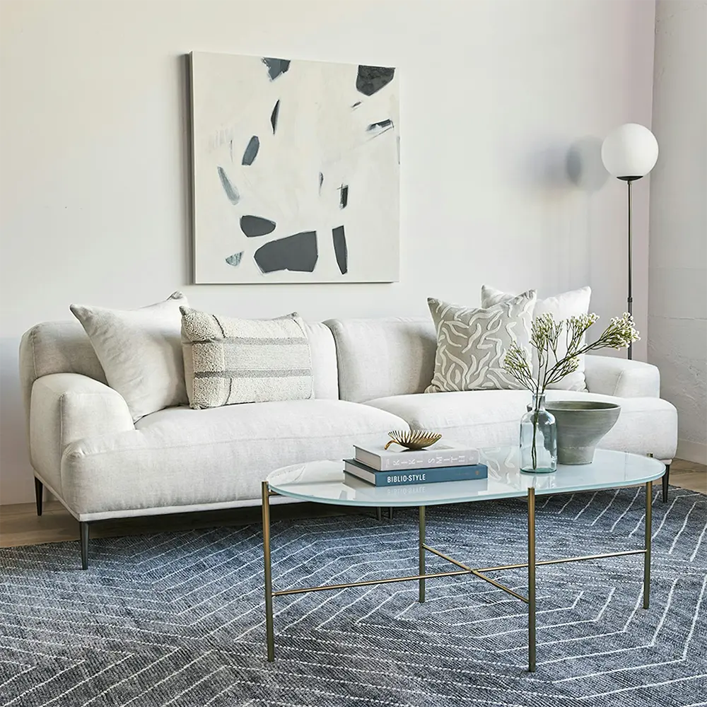 Modern living room with a white sofa, soft cushions and glass coffee table.