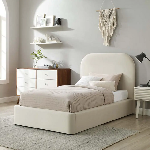 Beige upholstered bed in a bedroom with shelves, lamp, and decor.
