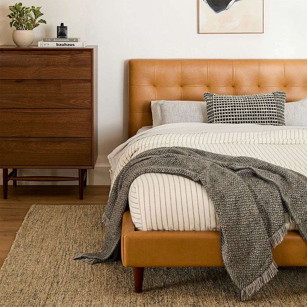 Bedroom with a brown upholstered bed, wooden dresser, and decorative items.