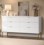 White dresser with gold legs in a room with decor elements like a lamp, painting, and vase.