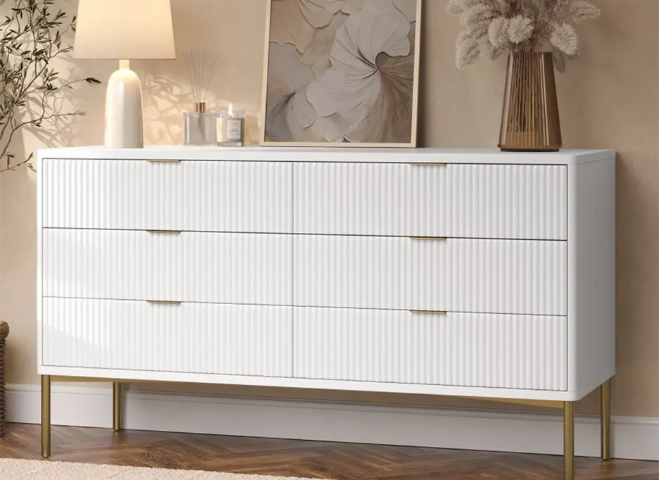 White dresser with gold legs in a room with decor elements like a lamp, painting, and vase.