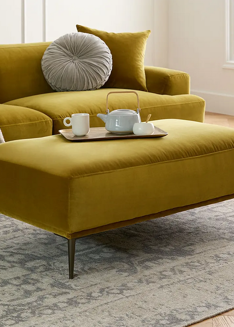 Yellow sectional sofa with a matching ottoman in a living room setting.