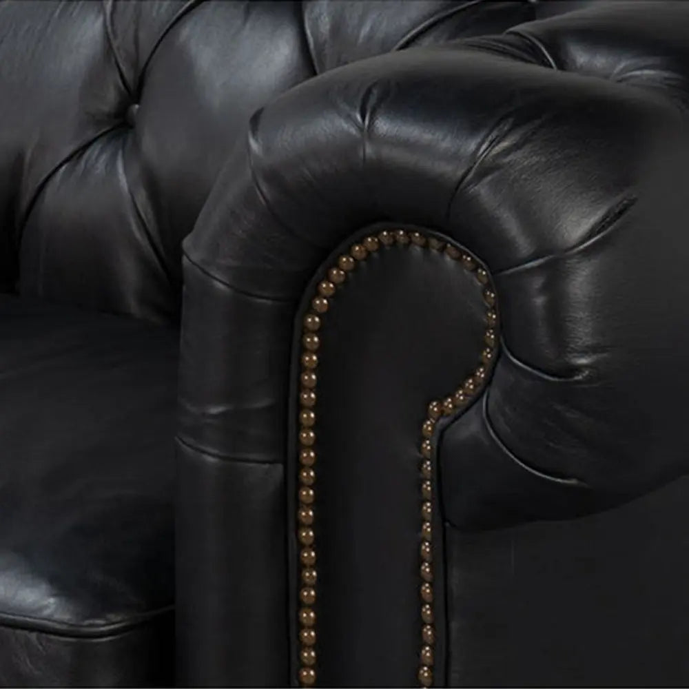 Close-up of a black leather sofa with tufted backrest and decorative nailhead trim.