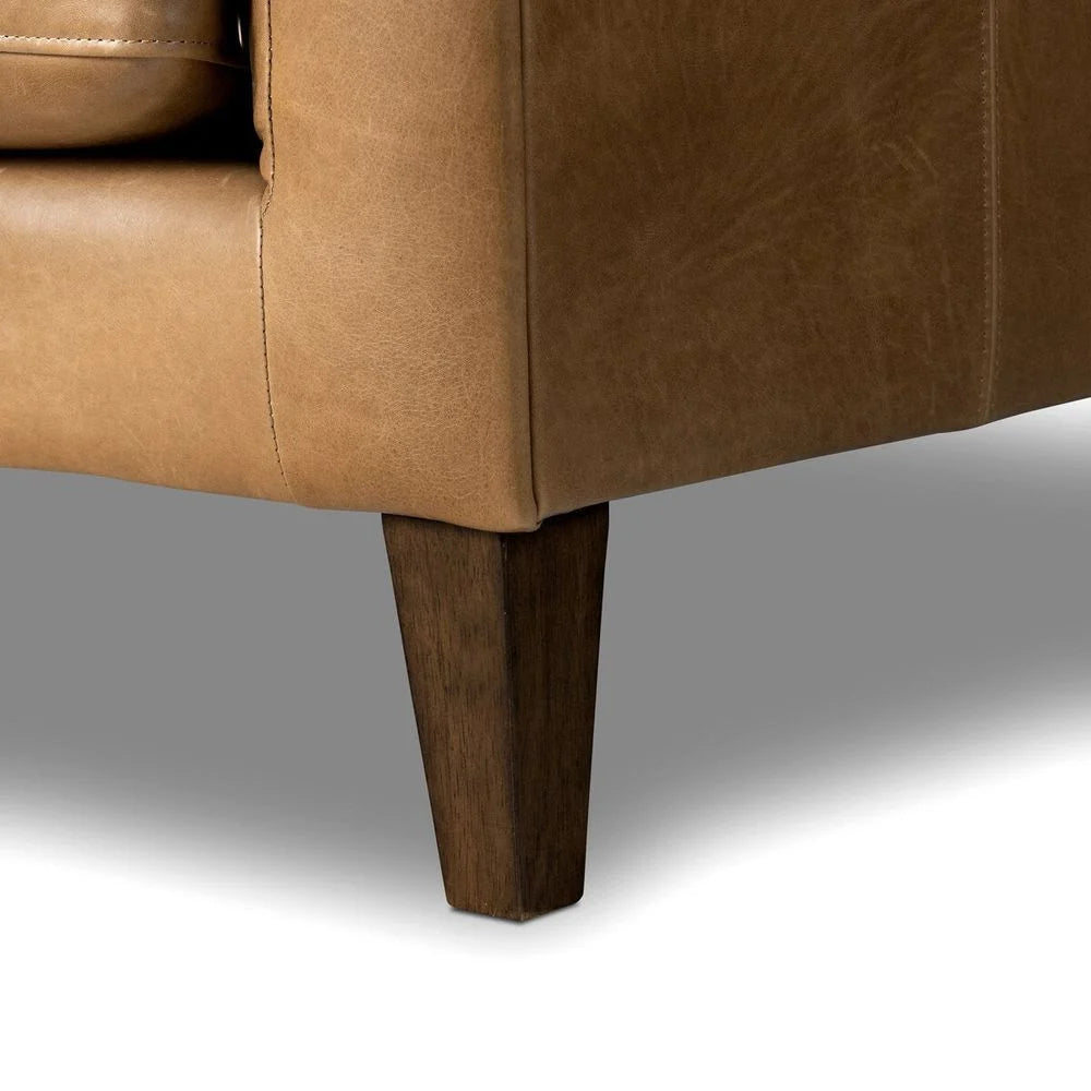 Close-up of a brown leather sofa with wooden legs on a gray background