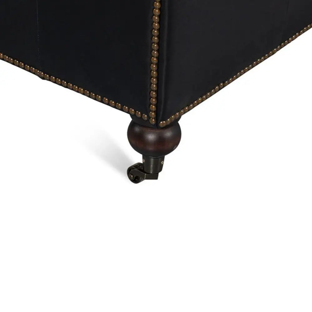 Close-up of a black upholstered sofa with brass nail head trim on a white background