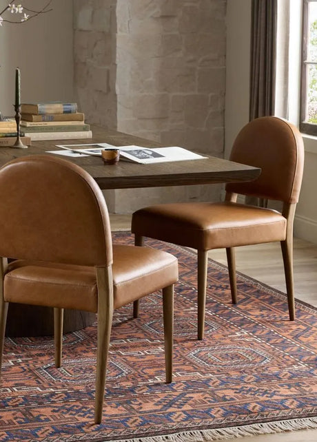 Two brown leather chairs in front of a wooden table on a patterned rug.
