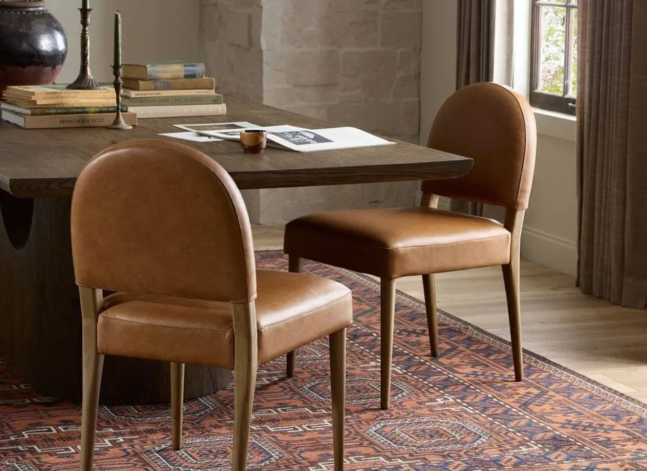 Two brown leather chairs in front of a wooden table on a patterned rug.