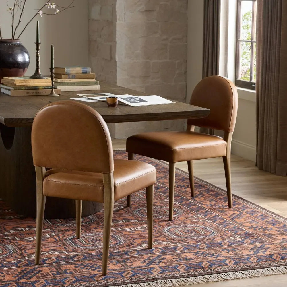 Two brown leather chairs in front of a wooden table on a patterned rug.